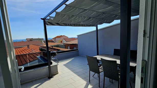 Una terrazza sul tetto con tavolo e sedie, un barbecue e vista sulla città.