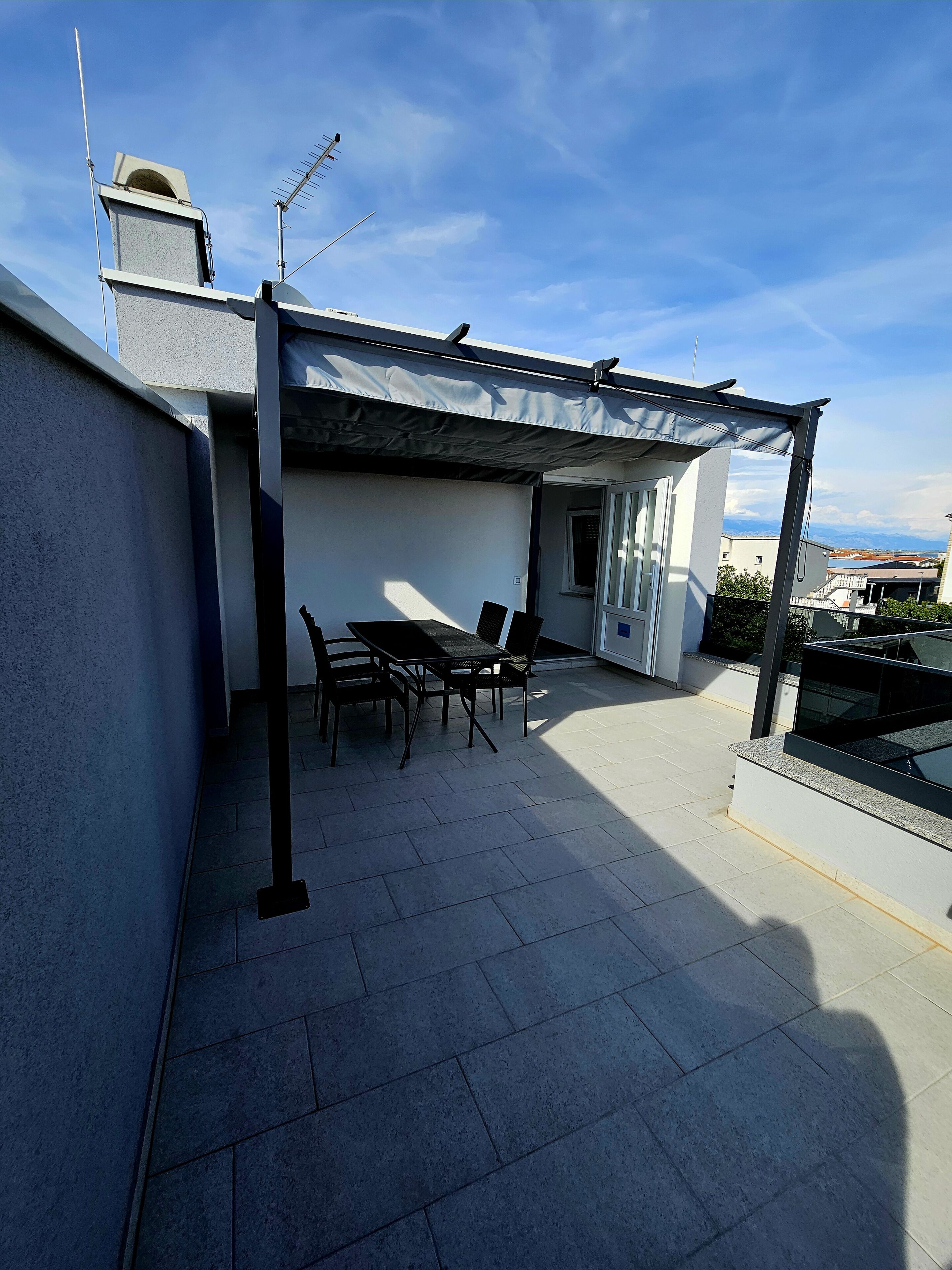 A rooftop terrace with a table and chairs, a pergola, and a view of the surrounding buildings.