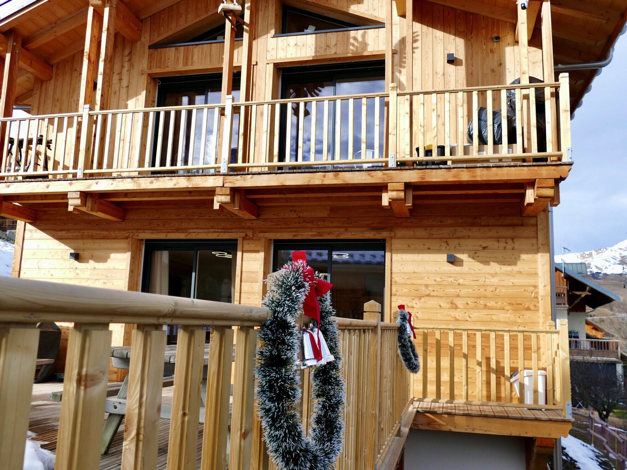A wooden chalet with a balcony, wooden railings, and a view of snow-capped mountains.
