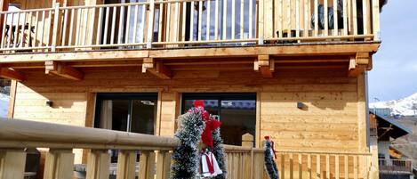 A wooden chalet with a balcony, wooden railings, and a view of snow-capped mountains.