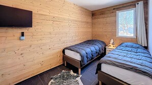 Une pièce aux murs en bois, avec deux lits, un téléviseur fixé au mur, une fenêtre donnant sur un beau paysage et un tapis sur le sol.