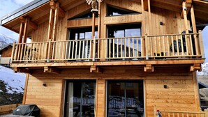 Une cabane en bois dotée d’un balcon, de grandes fenêtres et offrant une vue sur la montagne.
