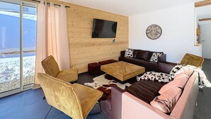 Un salon moderne avec un mur en bois, un téléviseur à écran plat, un canapé agrémenté de coussins à motifs et une grande fenêtre avec des rideaux.
