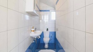 A narrow bathroom with white and blue tiles, a white sink, and a toilet. - Villa Nicole Gennadi (2W76+JJ South Rhodes, Greece)