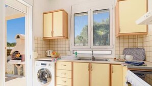 A compact kitchen with a washing machine, a sink, and a window with a view of greenery. - Villa Nicole Gennadi (2W76+JJ South Rhodes, Greece)
