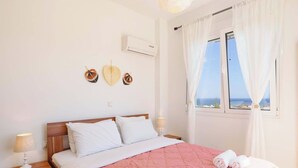 A bedroom with a bed, bedside lamps, a window with curtains, and wall decorations. - Villa Nicole Gennadi (2W76+JJ South Rhodes, Greece)