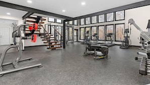 Un gimnasio moderno con diverso equipamiento de ejercicio, ventanas amplias y una escalera.