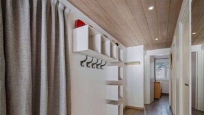 Een gang met houten vloer, witte wanden en een plafond met houten balken. Er staan witte bergkasten en er hangen haken aan de muur.