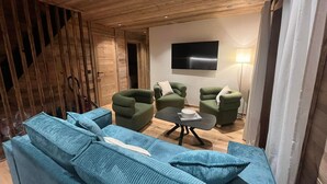 Ein modernes Wohnzimmer mit Holzboden, einem großen Flachbildfernseher und grünen Polster-Sofas.