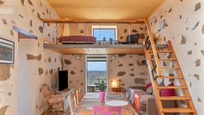 Ein kompakter Wohnraum mit Schlafgalerie, einem Esstisch mit Stühlen, einer Couch, einem Fernseher und einer Treppe.