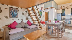 Ein Wohnzimmer mit Sofa, Couchtisch und Essbereich mit Stühlen. Eine Leiter lehnt an der Wand.