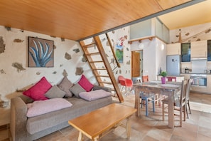 Un salon comprenant un canapé, une table basse et un coin repas avec des chaises. Une échelle est appuyée contre le mur.