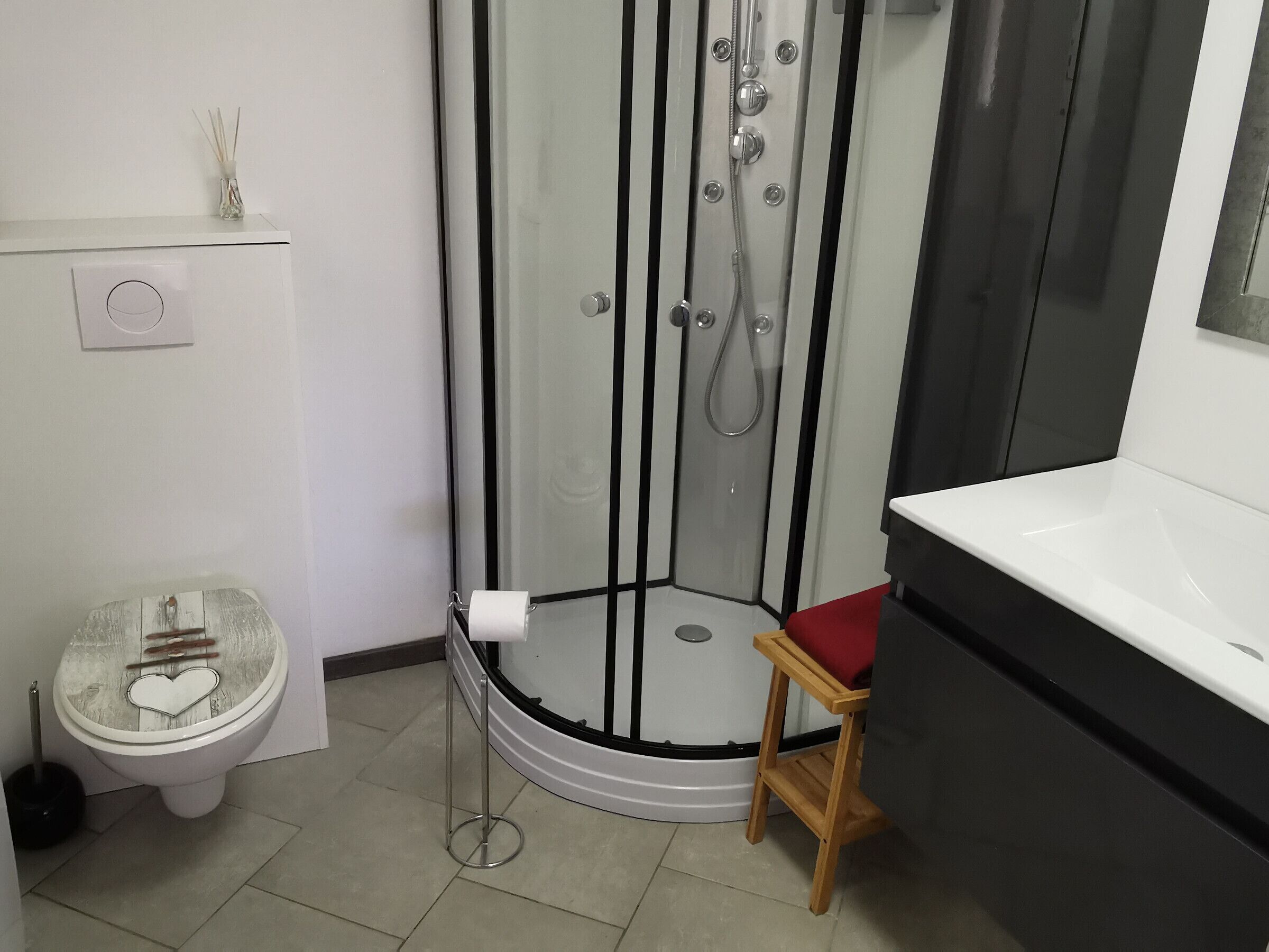 A bathroom with a glass-enclosed shower, a toilet with a wooden seat, and a small wooden stool.