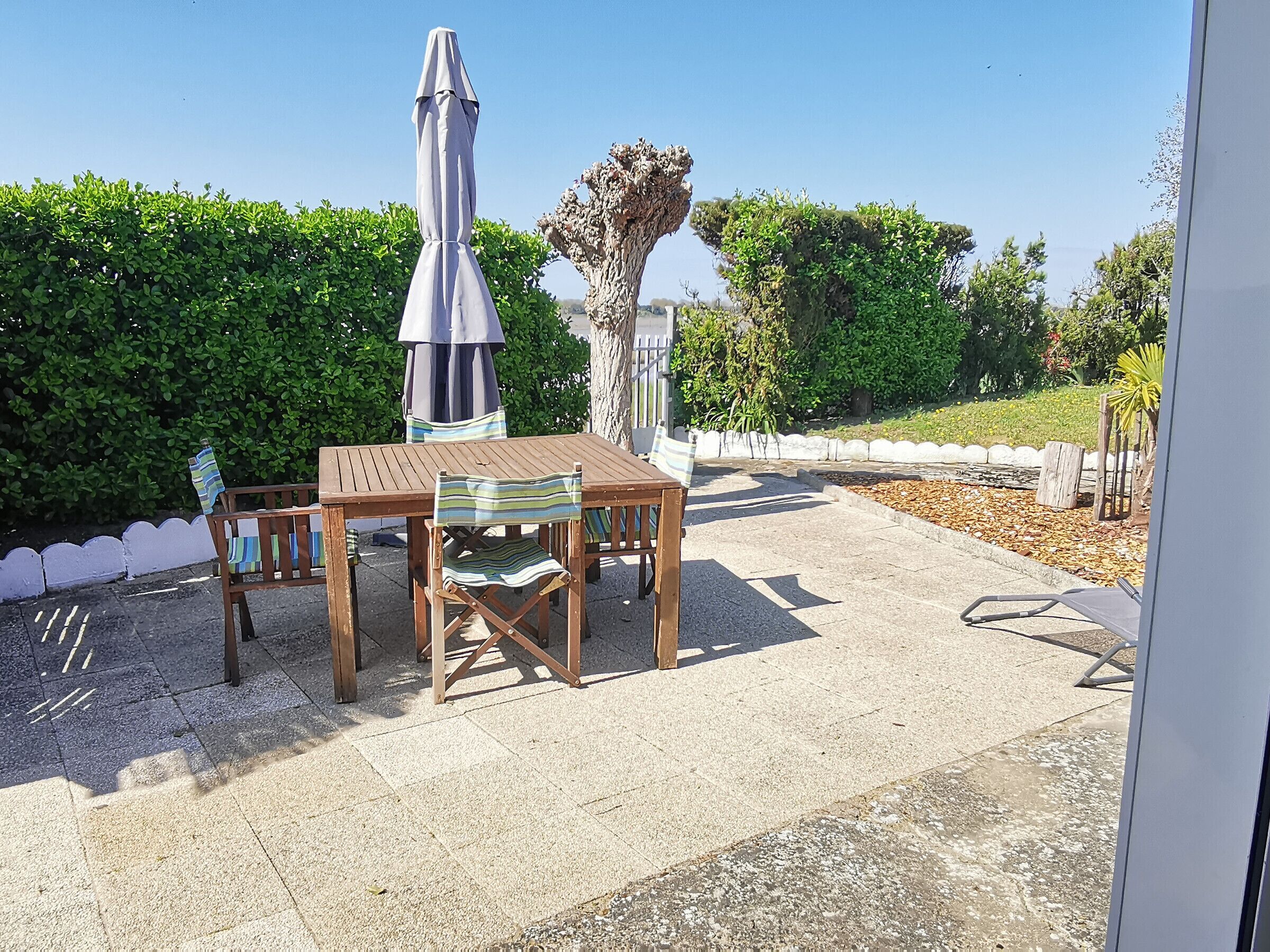 Une terrasse extérieure avec une table et des chaises en bois, un parasol en métal et un mur en pierre.