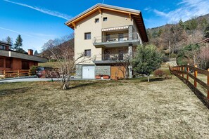 A two-story building with a balcony, a stone foundation, and a wooden fence.