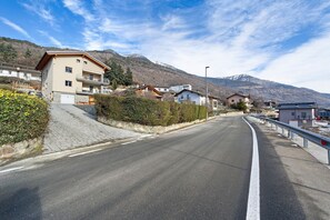 Eine Wohnstraße mit Häusern, blauem Himmel und Bergen im Hintergrund.