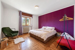 Ein Schlafzimmer mit einem Bett, einem Sessel, einem Hängesessel, einem Heizkörper und einem Fenster.