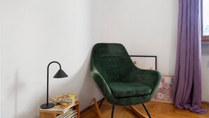Une pièce avec un fauteuil vert, un lampadaire noir, une table d’appoint en bois avec des livres et un rideau violet.