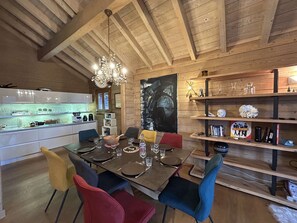 A dining area with a wooden ceiling, a chandelier, a kitchen with white cabinets, and a bookshelf with various items. - Spacious 5-room apartment for 8 people in Méribel with private parking (Méribel)