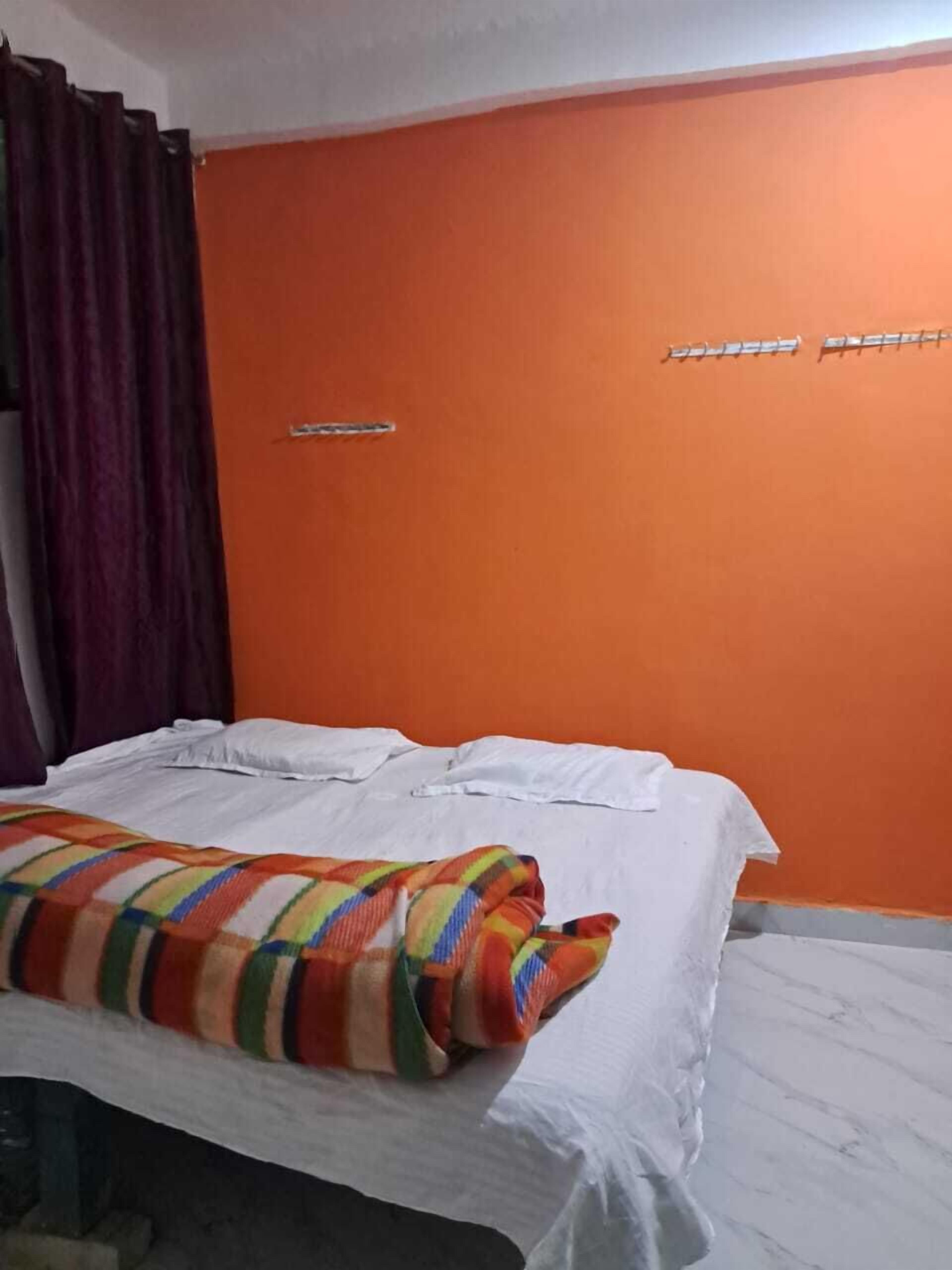 Een kamer met een oranje wand, een bed met witte lakens en een kleurrijke gestreepte deken.