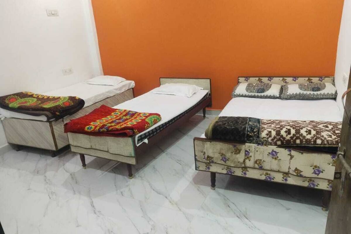 Una habitación con tres camas individuales, cada una con un edredón de estampado diferente. El suelo es de mármol blanco y las paredes son anaranjadas.