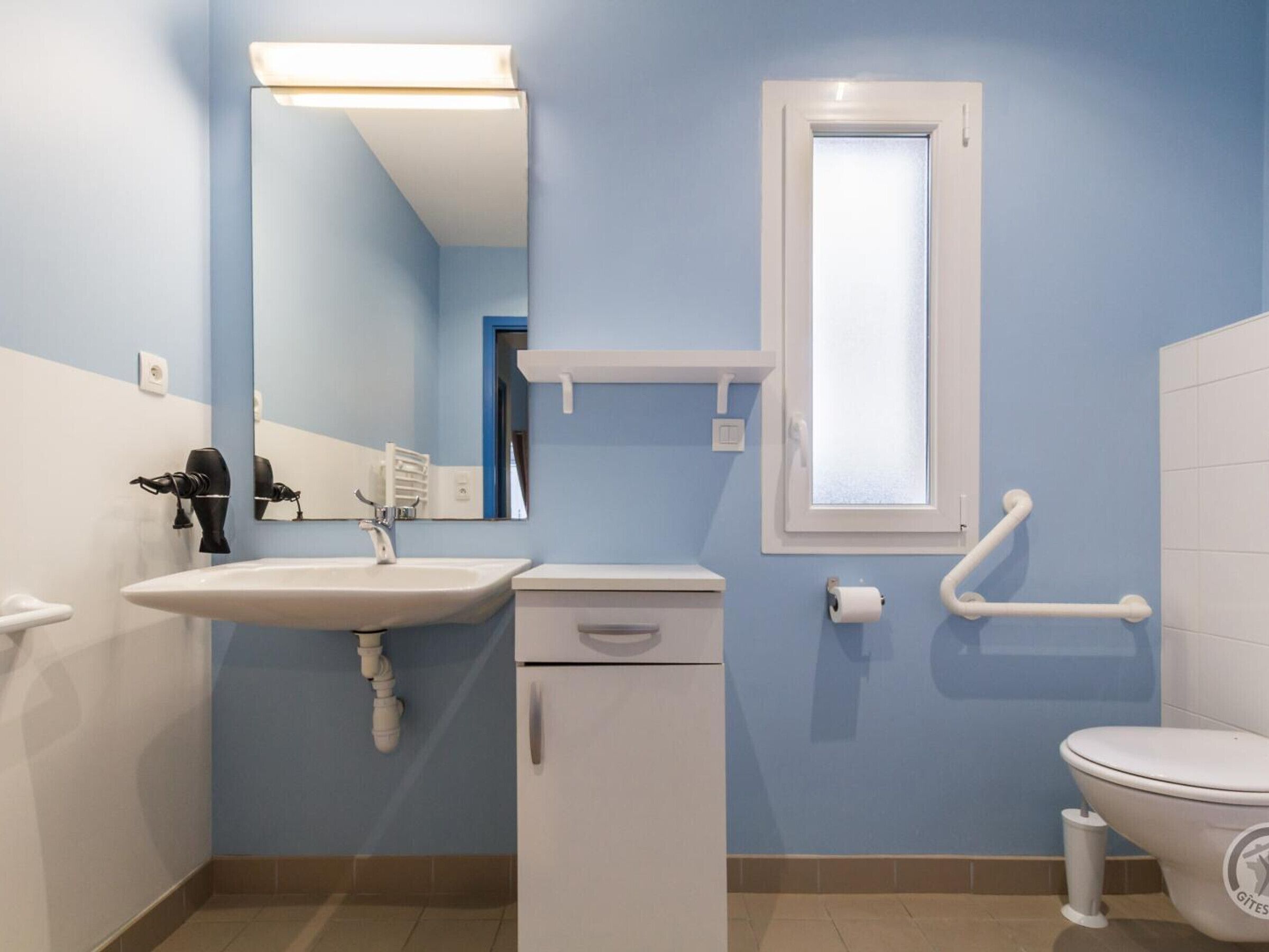 Un baño con lavamanos, espejo, inodoro y barras de apoyo.