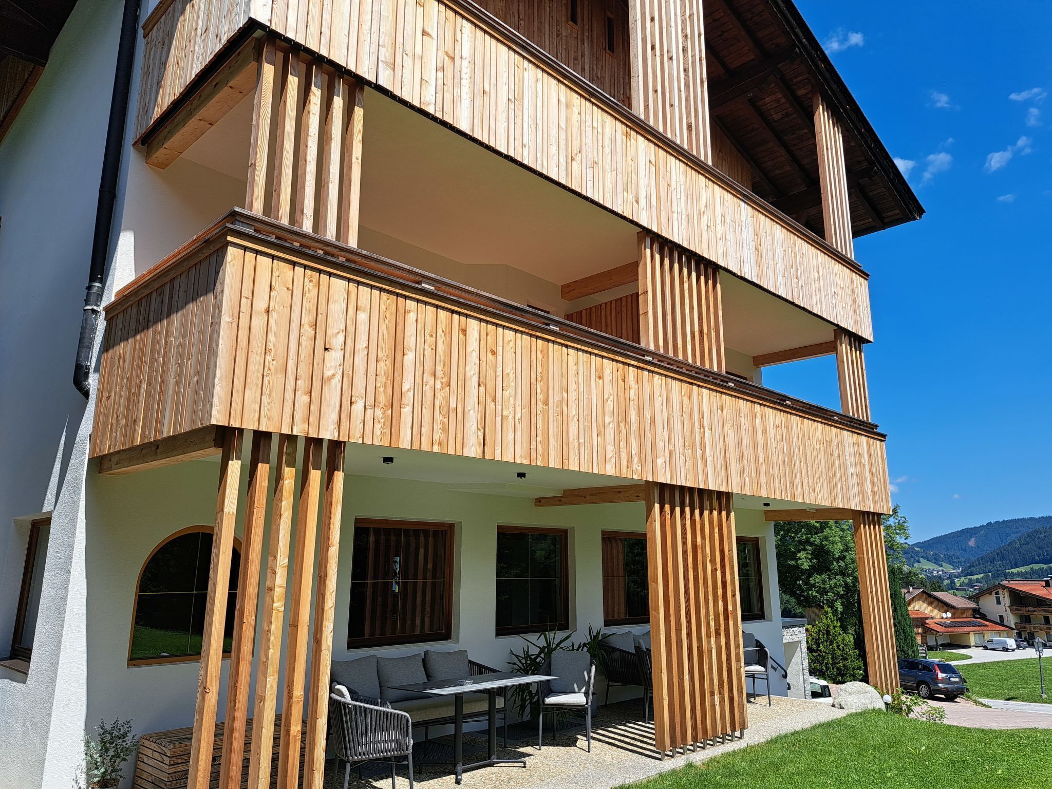Una casa a due piani in legno con un balcone, posti a sedere all'aperto e vista sul paesaggio circostante.