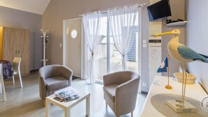 A modern room with a large window, two armchairs, a small table, a TV mounted on the wall, and a decorative seagull sculpture. - Accessible studio near beach, pets allowed (Siouville-Hague)
