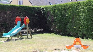 A playground with a slide and climbing structure, surrounded by a hedge and a house in the background. - Accessible studio near beach, pets allowed (Siouville-Hague)