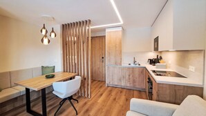 Una cocina moderna con armarios de madera, estufa integrada y un lavamanos. Hay un comedor con una mesa de madera y una silla blanca.
