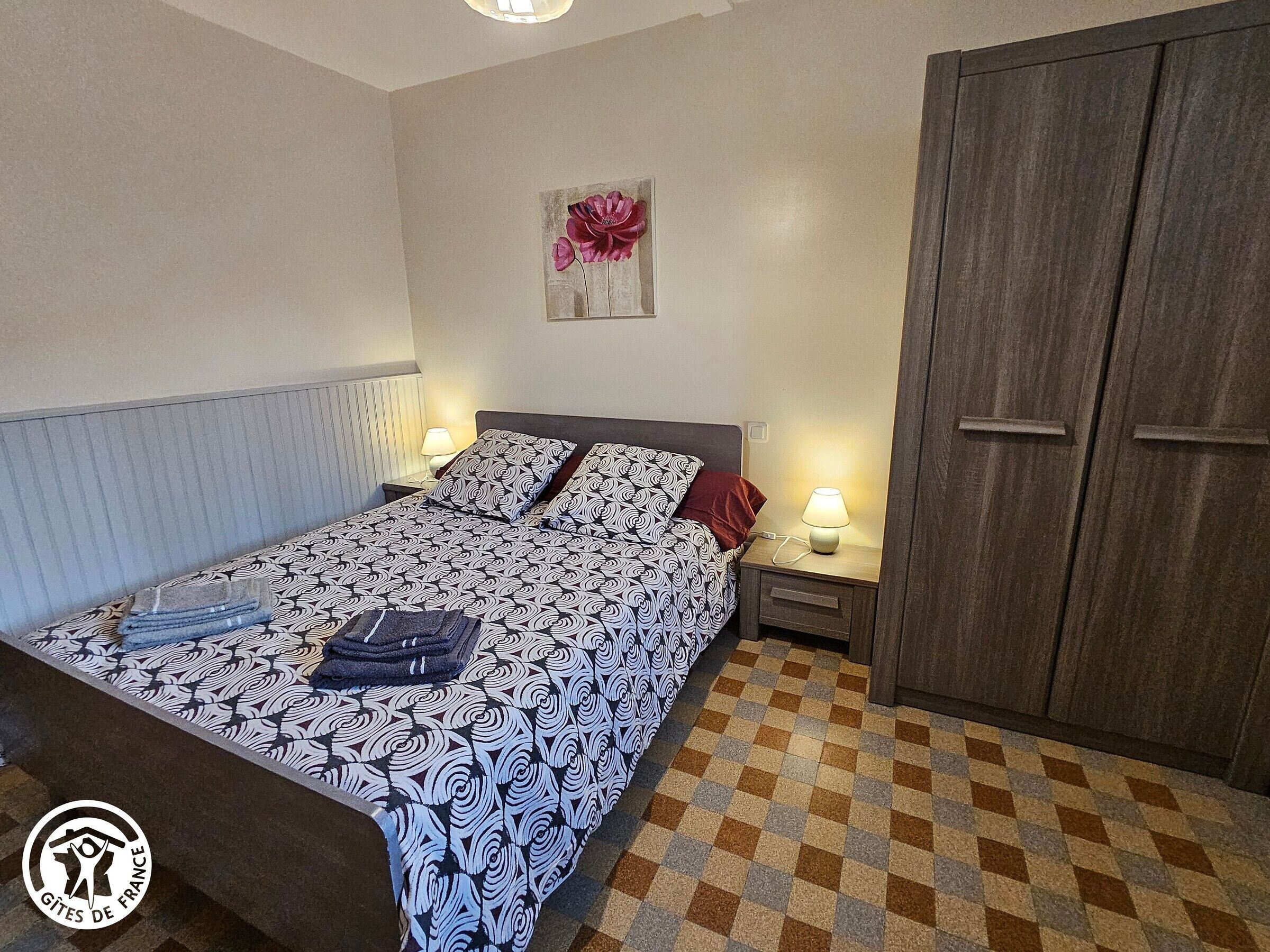 A bedroom with a bed, two bedside tables, a nightstand, a wardrobe, and a wall-mounted artwork.