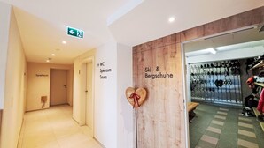 Corridoio di un hotel con indicazioni per 'Spielraum' e 'Sauna', e un'area dedicata a 'Sci & Scarponi da montagna' con scarponi da sci e scarpe.