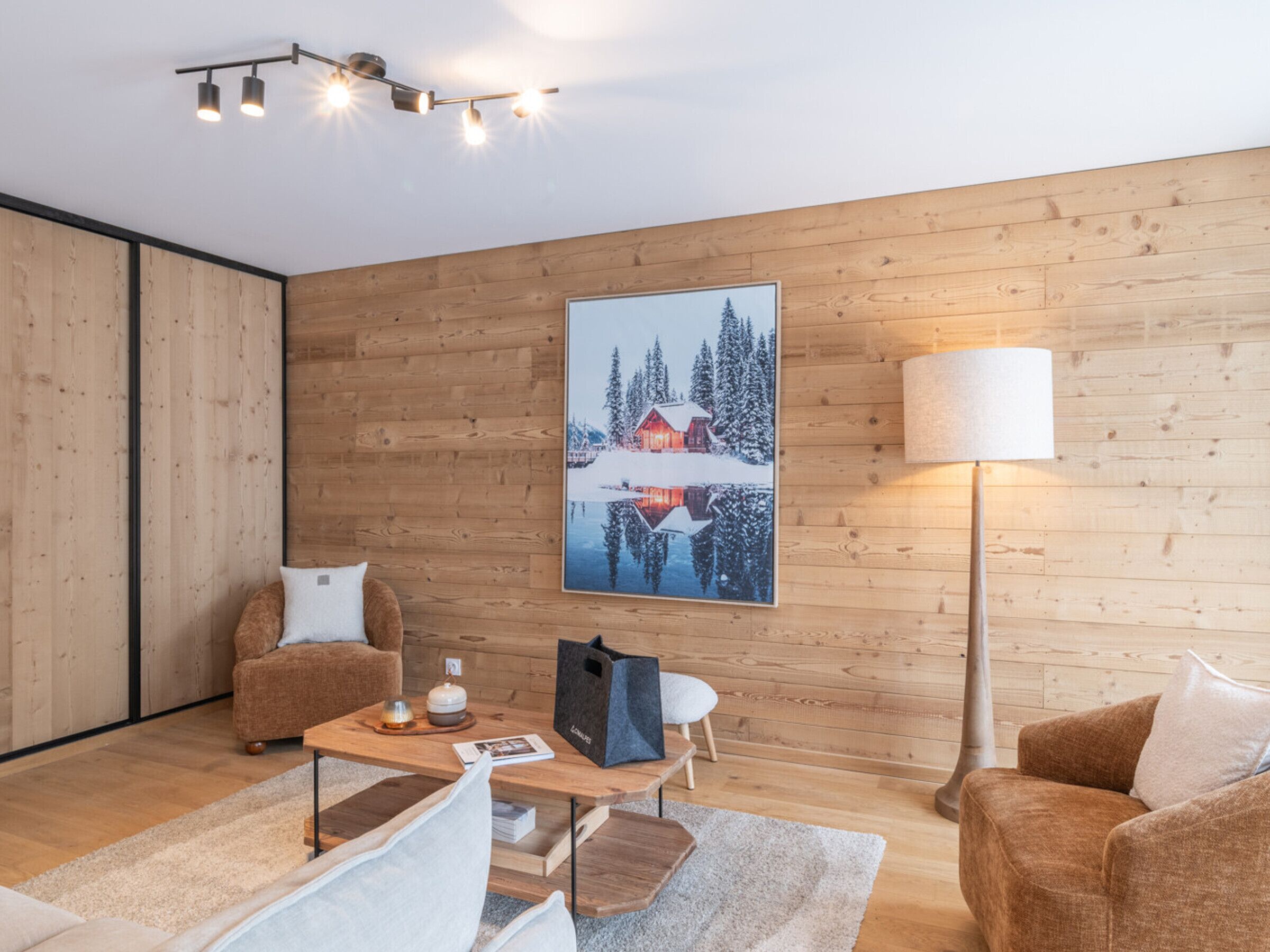 A modern living room with wooden walls, a large painting of a snowy landscape, a sofa, a coffee table, and a floor lamp.