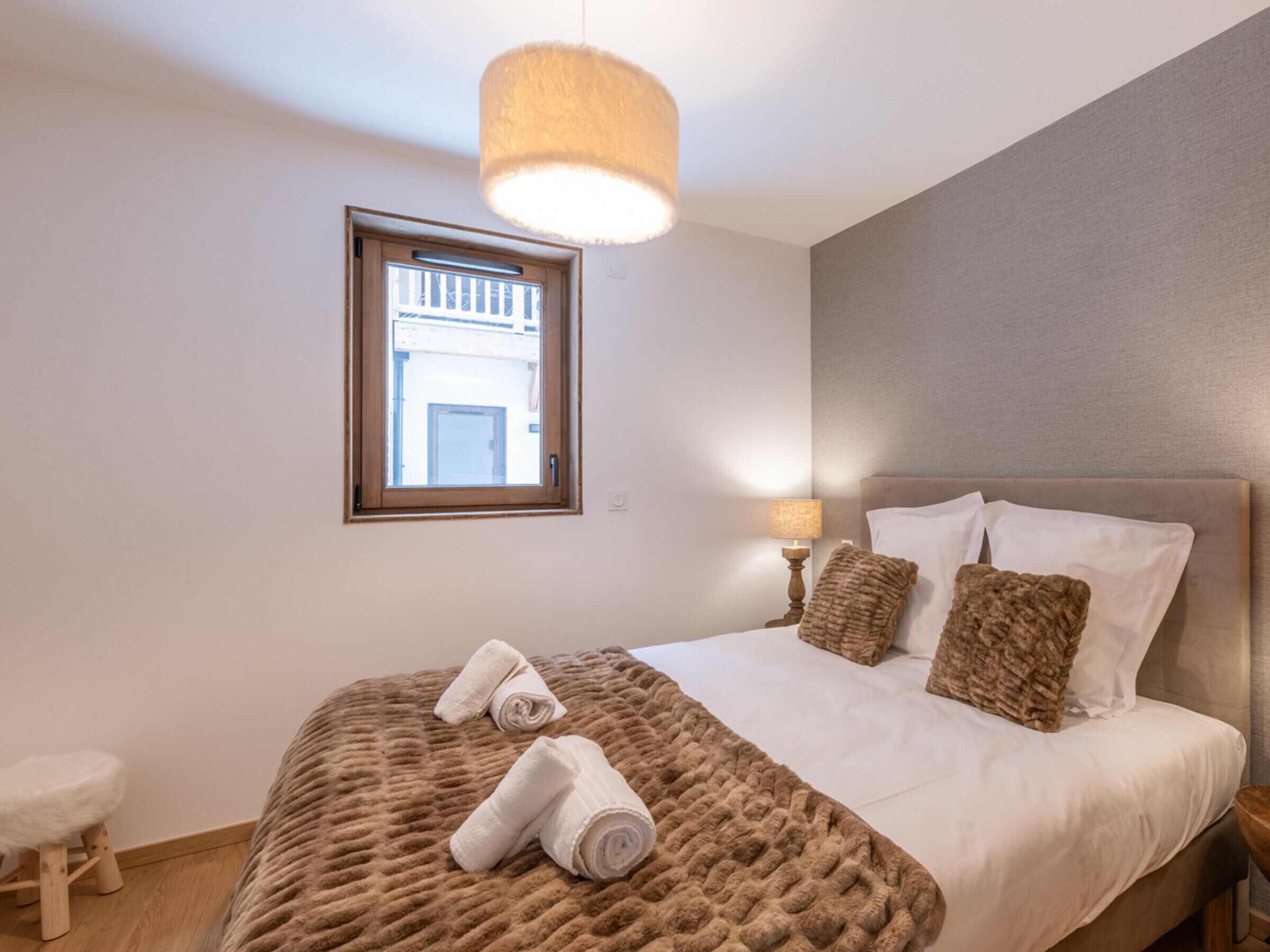 Una camera da letto con un letto grande, una finestra, una lampada da comodino e uno sgabello.