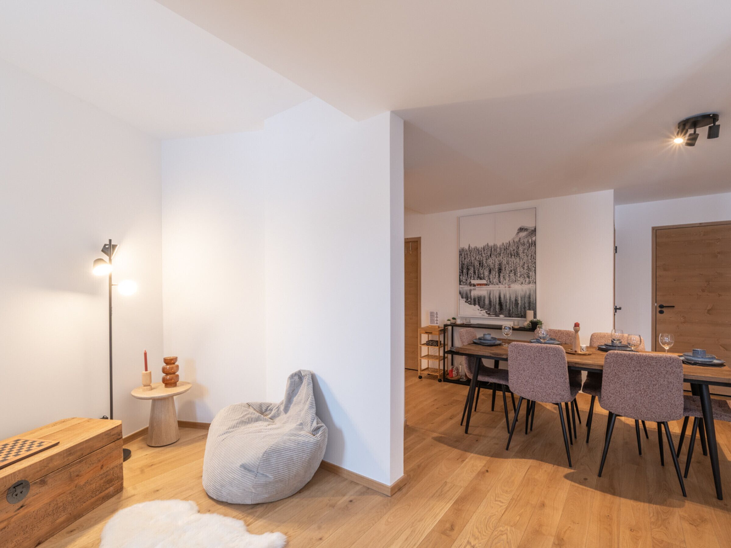 A modern dining area with a wooden table, chairs, and a large landscape painting on the wall.