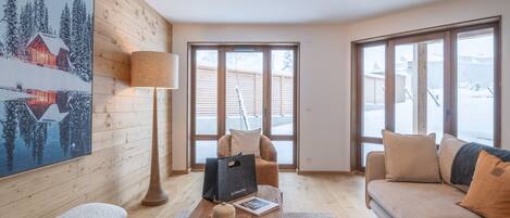 Uma sala de estar aconchegante com piso de madeira, uma janela grande, um sofá, uma mesa de centro e um quadro na parede.