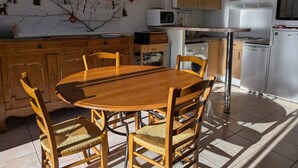 Cucina con mobili in legno, tavolo da pranzo con sedie, microonde, lavatrice e frigorifero.