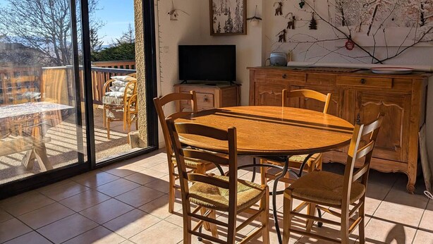 Zona pranzo con tavolo e sedie in legno, televisione e vista su un patio esterno attraverso una porta in vetro.