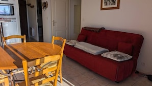 Un ambiente compatto con un tavolo da pranzo in legno e sedie, un divano rosso con cuscini e un quadro appeso alla parete.