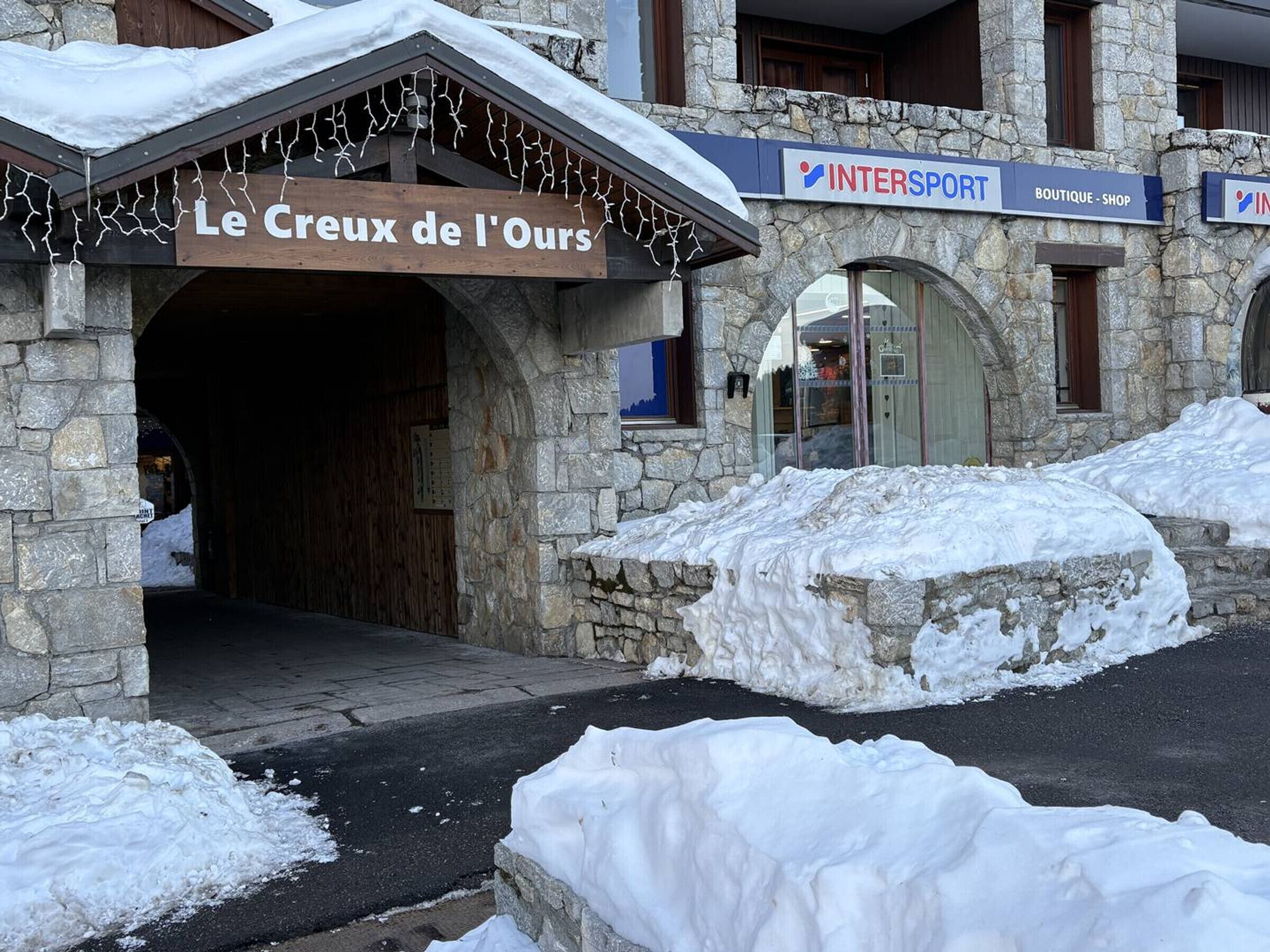 A stone building with a sign reading "Le Creux de l'Ours" and a sign for "INTERSPORT BOUTIQUE SHOP" above the entrance.