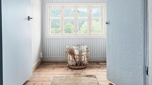 A narrow hallway with a window, a wicker basket, and a wooden floor.