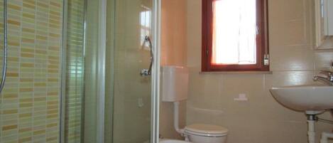 Un baño con cabina de ducha de vidrio, inodoro y lavamanos.