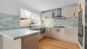 A modern kitchen with a large island, built-in oven, and a window providing natural light. - Panorama, Gerroa, South Coast (Gerroa)