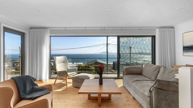 A modern living room with a sofa, armchair, and coffee table, large sliding glass doors leading to a balcony with a view of the sea. - Panorama, Gerroa, South Coast (Gerroa)