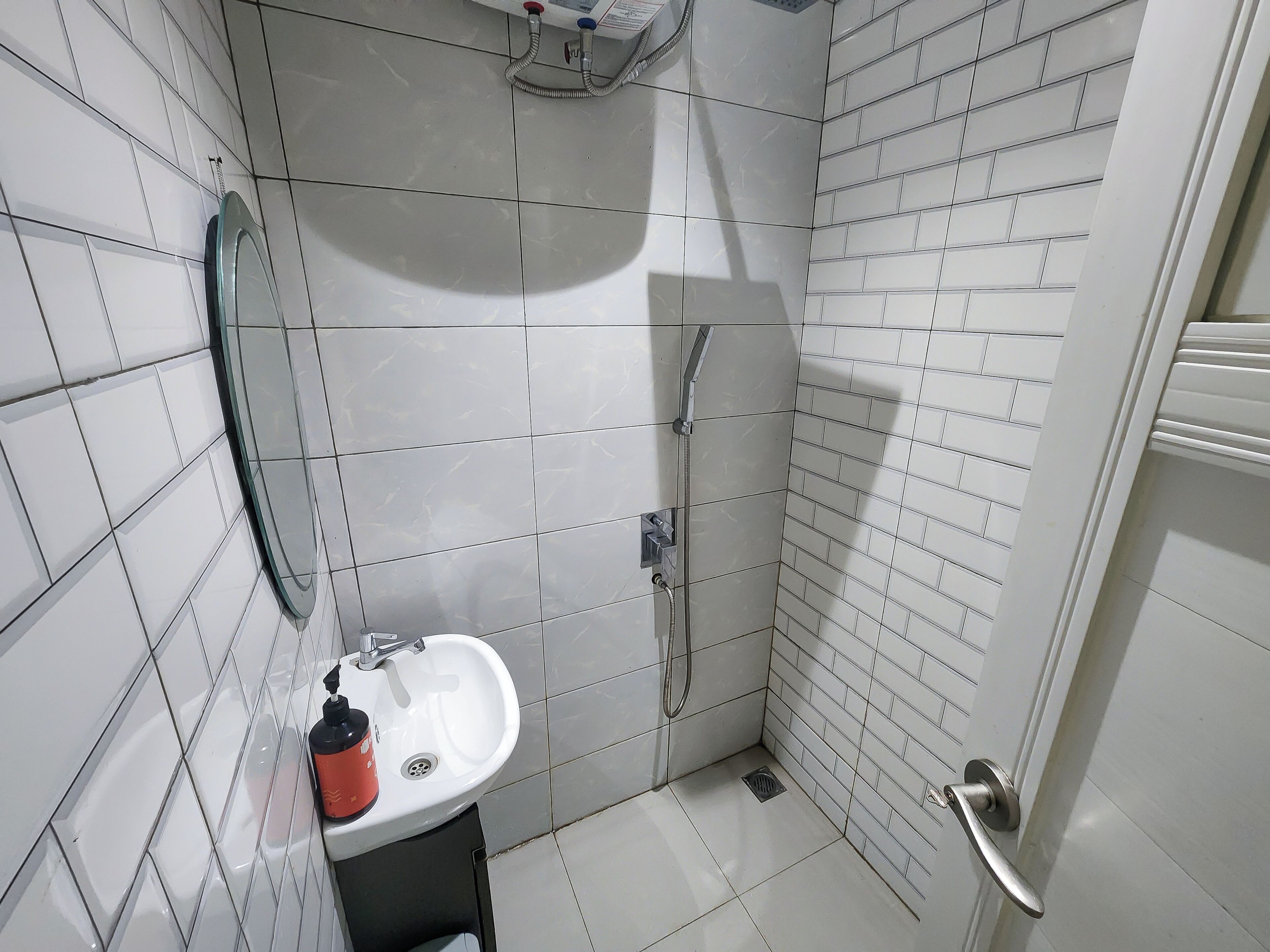 A small, tiled bathroom with a sink, a handheld showerhead, and a toilet.