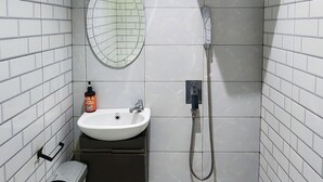 A small, modern bathroom with white tiles, a round mirror, a sink, a toilet, and a shower. - Pakuan Residence Hotel (Bogor)