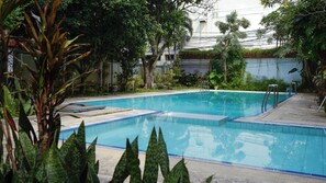 A swimming pool with clear blue water, surrounded by lush greenery and a white building in the background. - Pakuan Residence Hotel (Bogor)