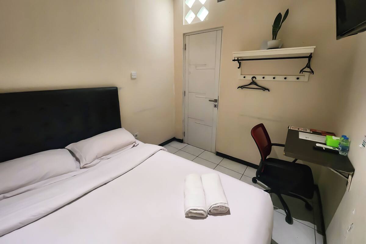 A hotel room with a bed, a desk, a chair, a TV, and a door.