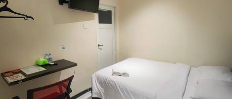 Une chambre d’hôtel avec un lit, un bureau et une chaise, un téléviseur fixé au mur et une porte.