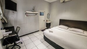 A hotel room with a bed, a desk, a chair, a TV, a sink, and an air conditioning unit. - Pakuan Residence Hotel (Bogor)